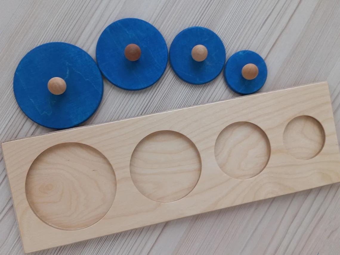 Montessori koka puzles dēlis ar četriem dažāda izmēra apļiem un rokturīšiem.
