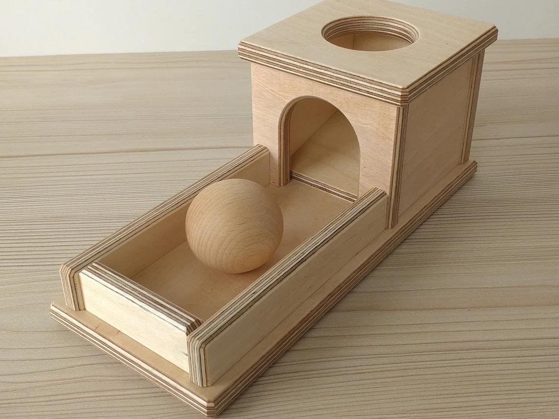 Montessori priekšmetu pastāvības kaste ar koka bumbiņu un bērza uztveršanas paplāti.